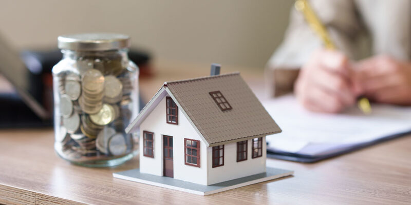 Toy house and coins on desk signing investment property loan