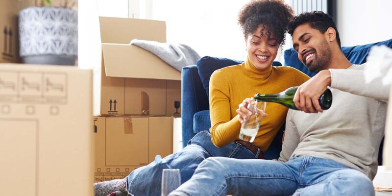 Couple with moving boxes drinking champagne to celebrate getting a great mortgage rate
