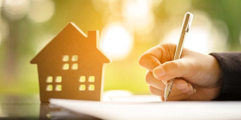 Signing a document with a toy house next to the papers