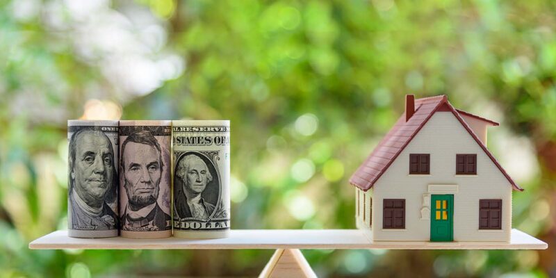 toy house and money on opposite sides of a scale